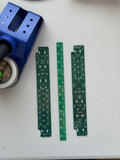 Two green printed circuit boards on a white surface with a blue tool.